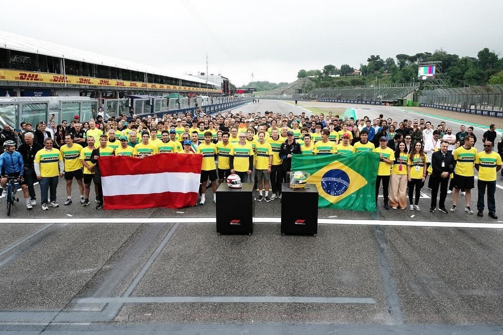 Formula One personnel pose for a group photo holding the Austrian and Brazilian flags during a tribute for Roland Ratzenberger and Ayrton Senna at the 2024 Emilia Romagna Grand Prix