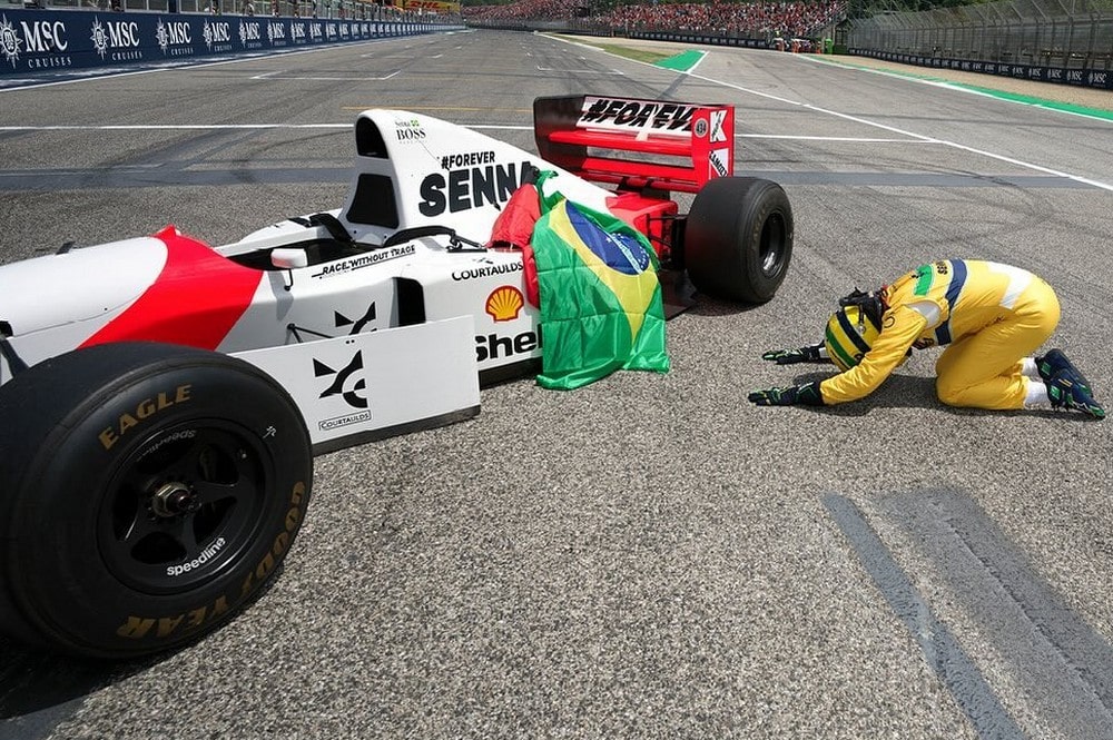 Sebastian Vettel kneels beside a Brazilian and Austrian flag draped over the McLaren MP4/8 during a tribute for Roland Ratzenberger and Ayrton Senna at the 2024 Emilia Romagna Grand Prix