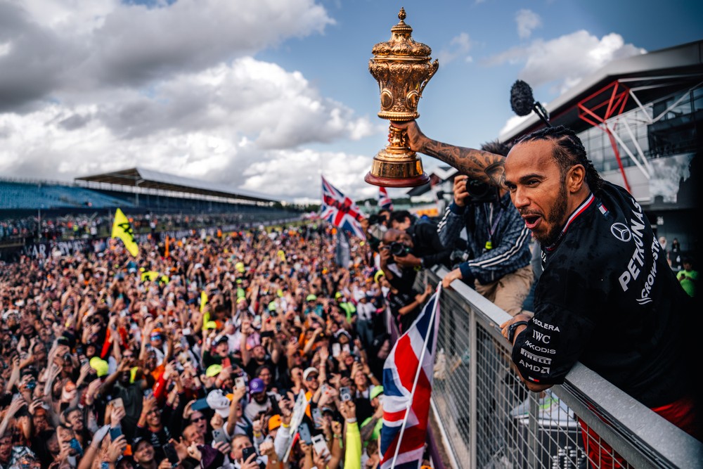 Lewis Hamilton holds up the 2024 British Grand Prix winner's trophy over a sea of fans