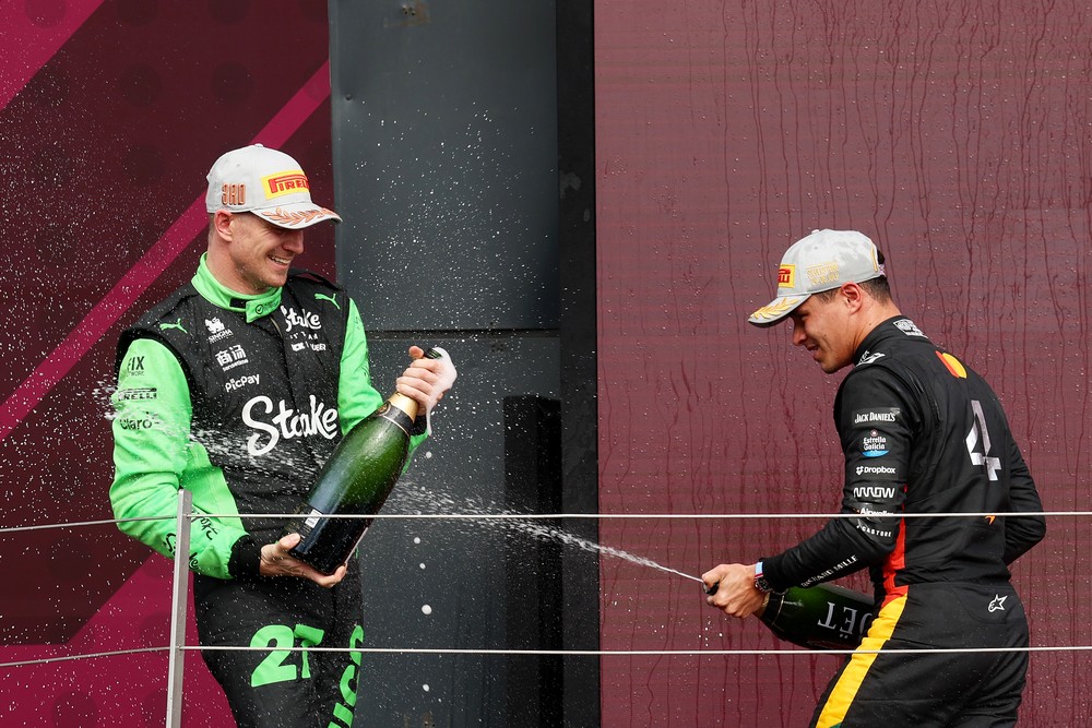 Lando Norris (right) sprays Nico Hulkenberg (left) with champagne on the podium after winning the 2025 British Grand Prix
